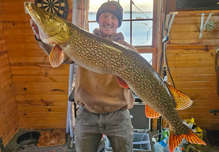 image of ice fisherman holding a huge northern pike caught during an ice fishing trip to lake of the woods